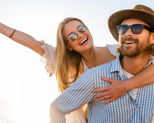 attractive happy couple laughing traveling in summer by sea, man and woman wearing sunglasses, boho hipster style fashion having fun together